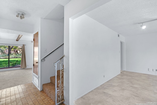 empty room with light carpet, beam ceiling, a textured ceiling, and rail lighting