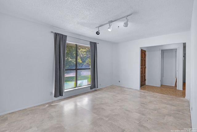 unfurnished room with a textured ceiling, light tile flooring, and rail lighting