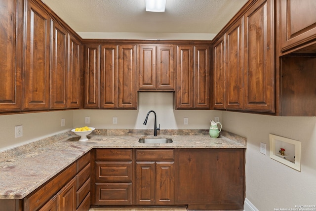 kitchen featuring a textured ceiling, sink, and light stone countertops