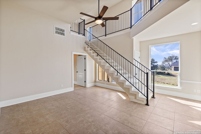 stairway with ceiling fan, light tile floors, and a high ceiling