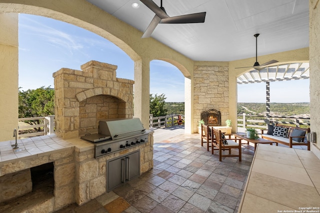 view of terrace featuring grilling area, an outdoor kitchen, an outdoor living space with a fireplace, and ceiling fan