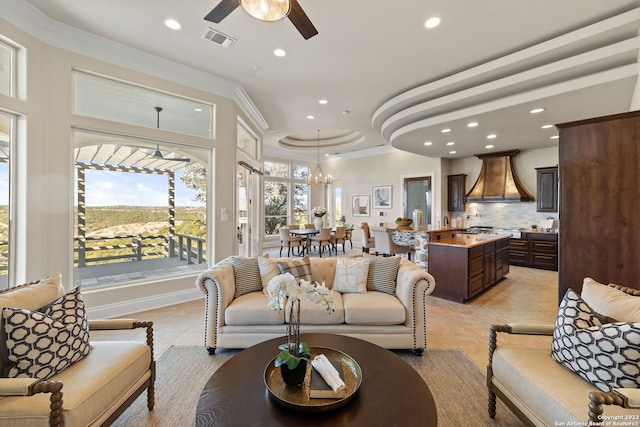 living room with ceiling fan with notable chandelier, a wealth of natural light, light tile flooring, and a raised ceiling