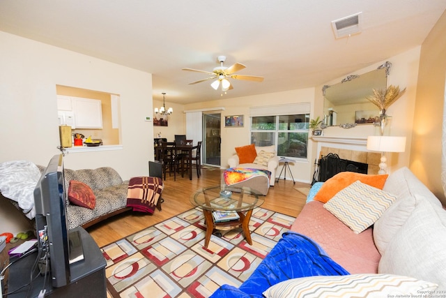 living room featuring a tiled fireplace, ceiling fan with notable chandelier, and light hardwood / wood-style flooring