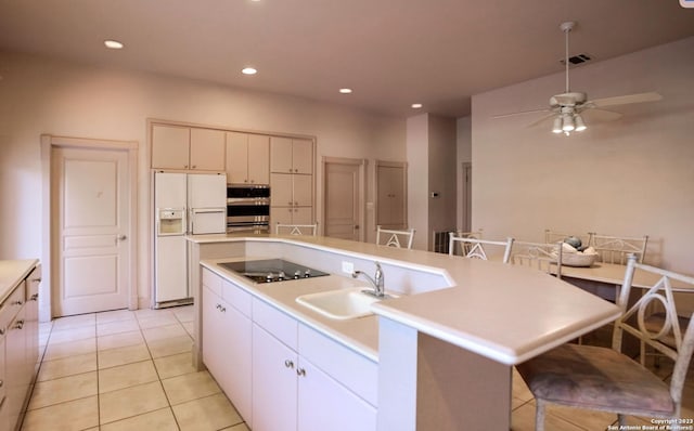 kitchen with white fridge with ice dispenser, stainless steel oven, sink, black electric cooktop, and a kitchen island with sink