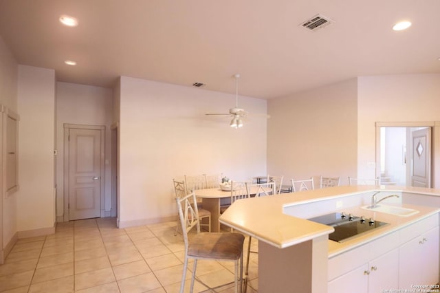 kitchen with ceiling fan, sink, light tile patterned floors, white cabinetry, and a breakfast bar area