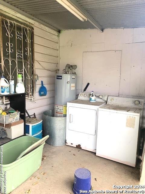 laundry area with laundry area, washing machine and dryer, wooden walls, and gas water heater