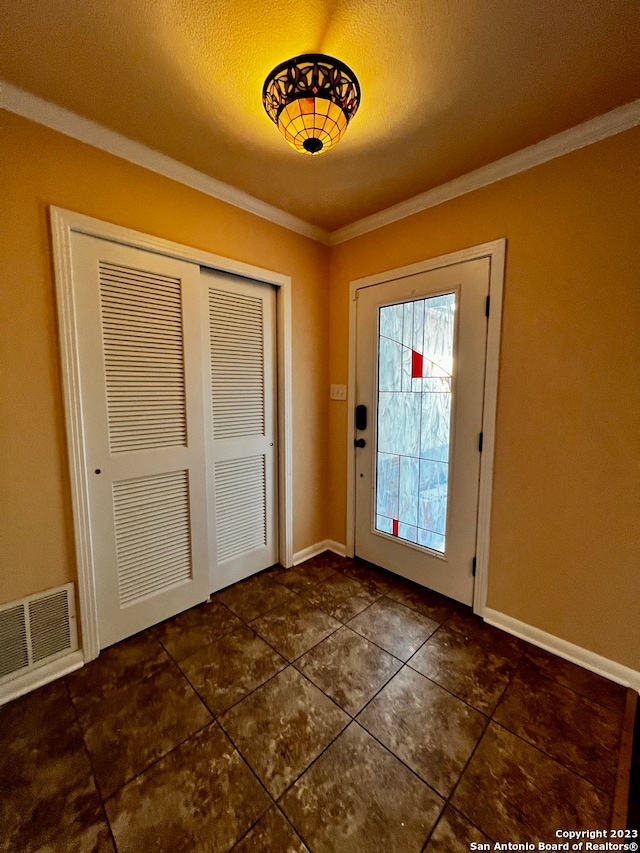 entryway with ornamental molding and dark tile patterned flooring