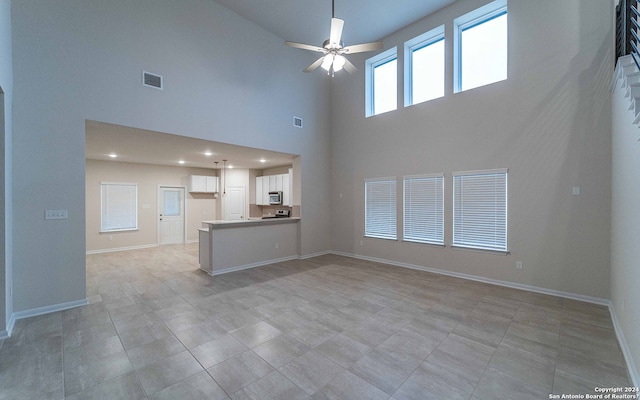 unfurnished living room featuring light tile patterned flooring, ceiling fan, and a towering ceiling