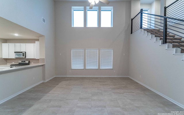 unfurnished living room featuring a high ceiling, ceiling fan, and light tile patterned floors