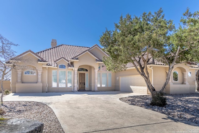 mediterranean / spanish-style home with a garage, driveway, a tile roof, a chimney, and stucco siding