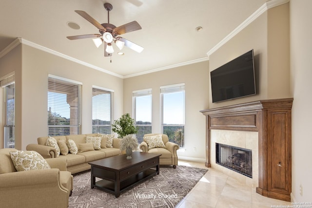 living room with ceiling fan, a tiled fireplace, baseboards, and crown molding