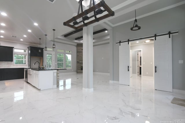 kitchen featuring ornamental molding, a barn door, a kitchen island with sink, and plenty of natural light