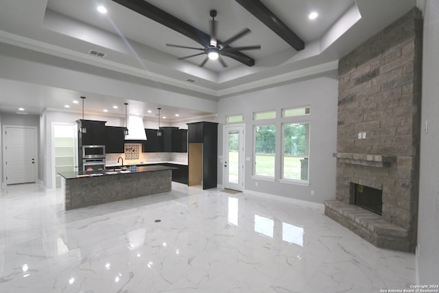 kitchen featuring a stone fireplace, beamed ceiling, oven, a kitchen island with sink, and backsplash