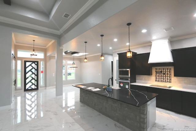 kitchen featuring a large island with sink, ornamental molding, custom range hood, and decorative backsplash