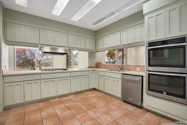 kitchen featuring stainless steel appliances, ventilation hood, light tile patterned floors, and a wealth of natural light