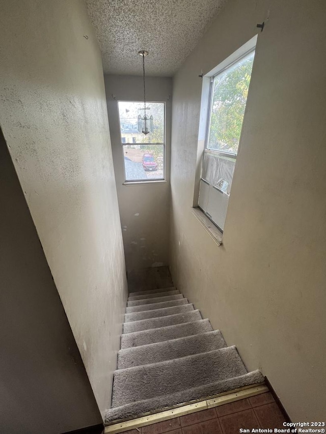 stairs with a chandelier and a textured ceiling