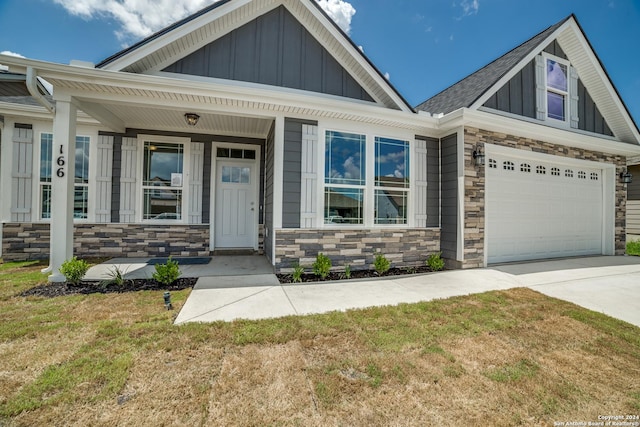 craftsman-style home with driveway, a garage, stone siding, covered porch, and board and batten siding