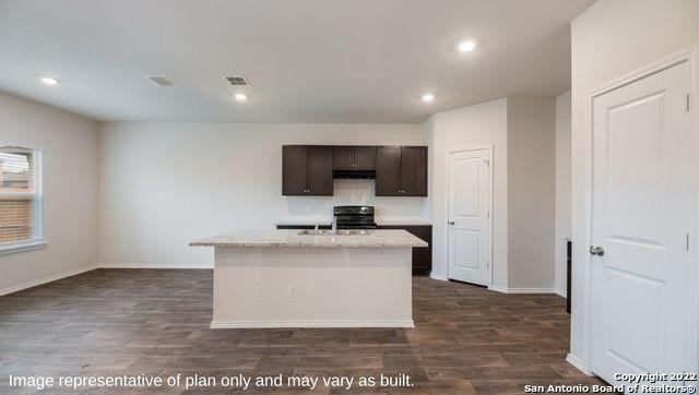 kitchen featuring stove, dark brown cabinetry, a center island with sink, and dark hardwood / wood-style floors