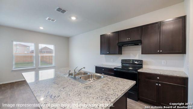 kitchen with light stone countertops, sink, a center island with sink, light hardwood / wood-style flooring, and black range with electric stovetop