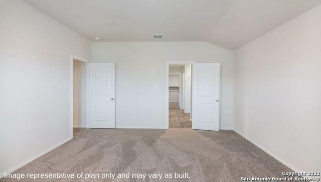 unfurnished bedroom featuring a walk in closet, light carpet, a closet, and lofted ceiling