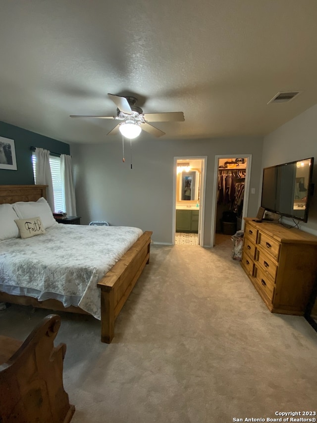 carpeted bedroom with a walk in closet, a textured ceiling, ceiling fan, connected bathroom, and a closet