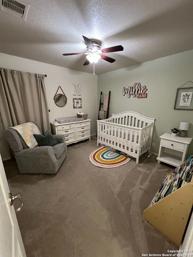 bedroom featuring a crib, a textured ceiling, dark colored carpet, and ceiling fan