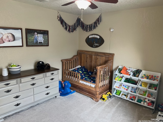 bedroom with a textured ceiling, ceiling fan, carpet, and a crib