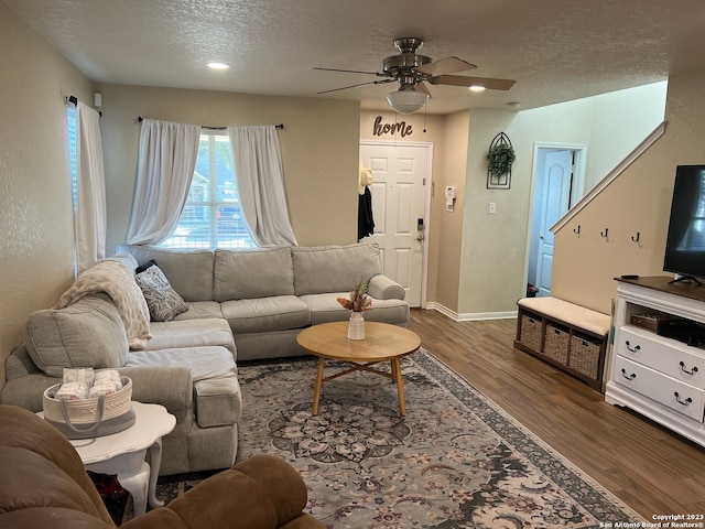 living room with a textured ceiling, ceiling fan, and dark wood-type flooring