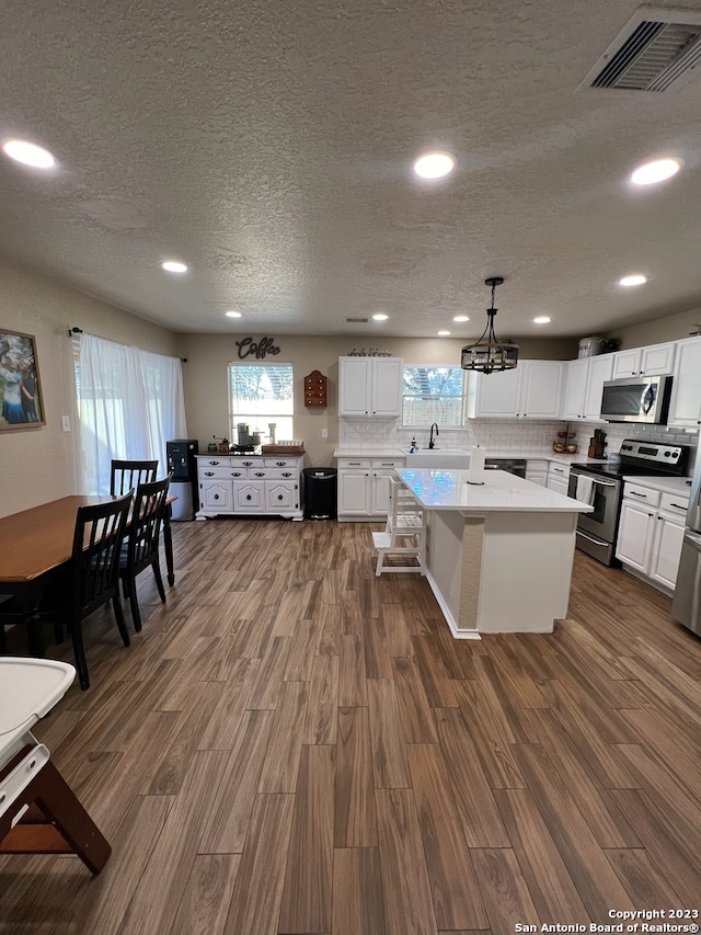 kitchen with dark wood-type flooring, decorative light fixtures, a kitchen island, white cabinetry, and stainless steel appliances