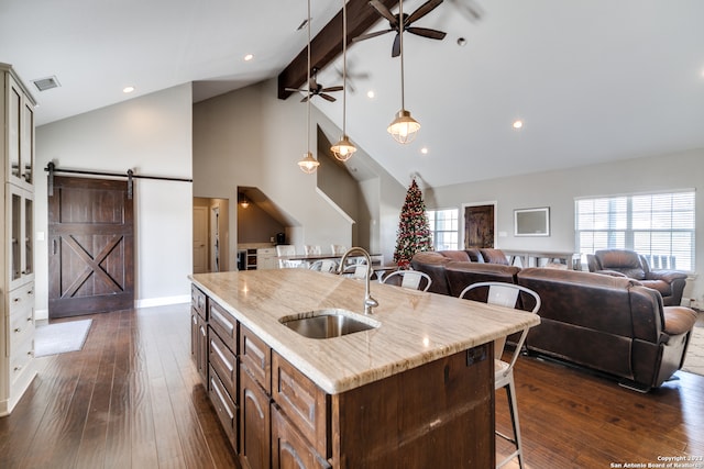 kitchen featuring beam ceiling, a kitchen island with sink, a barn door, ceiling fan, and dark hardwood / wood-style floors