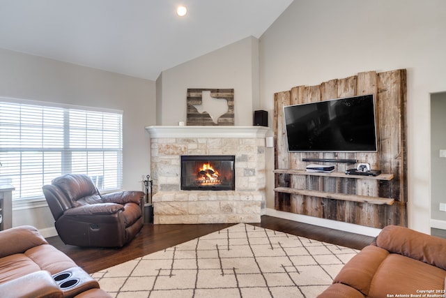 living room with a stone fireplace, wood-type flooring, and lofted ceiling