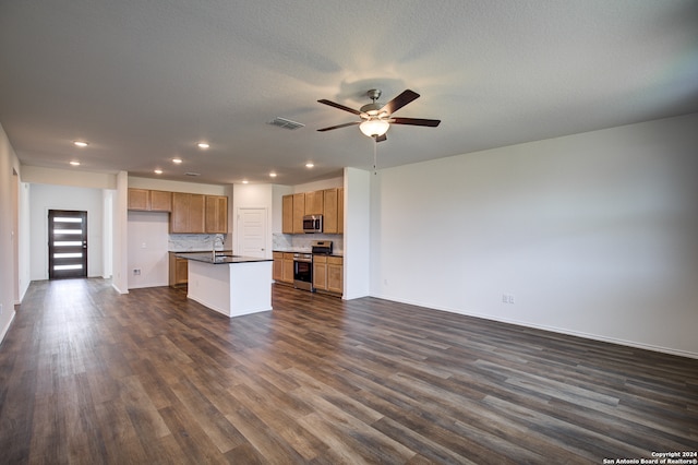 kitchen with sink, dark hardwood / wood-style flooring, backsplash, a kitchen island with sink, and appliances with stainless steel finishes