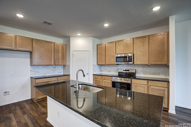 kitchen with sink, stainless steel appliances, dark hardwood / wood-style floors, dark stone counters, and a center island with sink