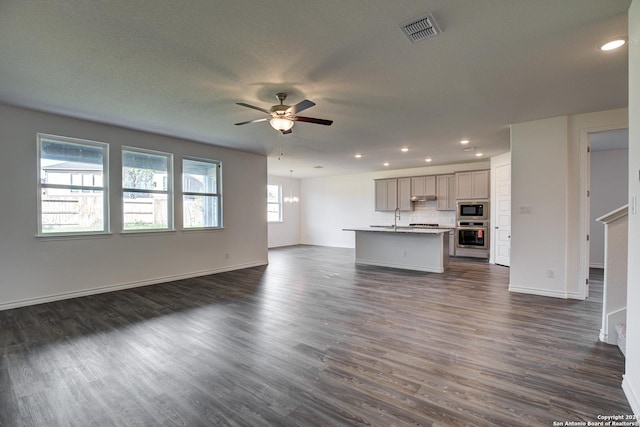 unfurnished living room with ceiling fan with notable chandelier, sink, and dark wood-type flooring