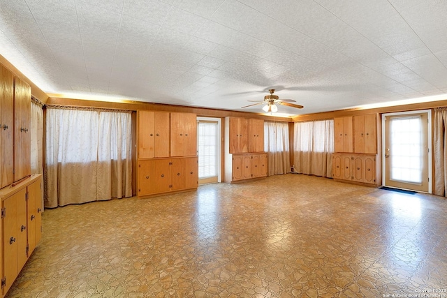 unfurnished living room with ceiling fan and wooden walls