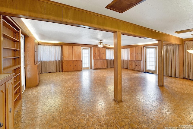 unfurnished living room with built in shelves, a textured ceiling, ceiling fan, and wood walls