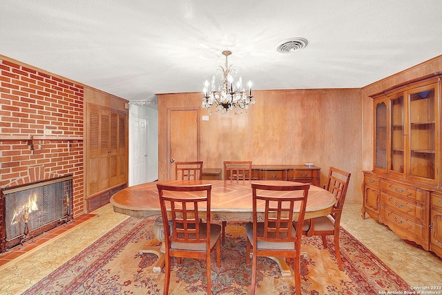 dining area featuring a notable chandelier, ornamental molding, a textured ceiling, a brick fireplace, and wood walls