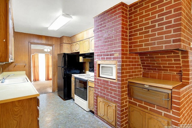 kitchen with black refrigerator, sink, range with electric cooktop, and wood walls