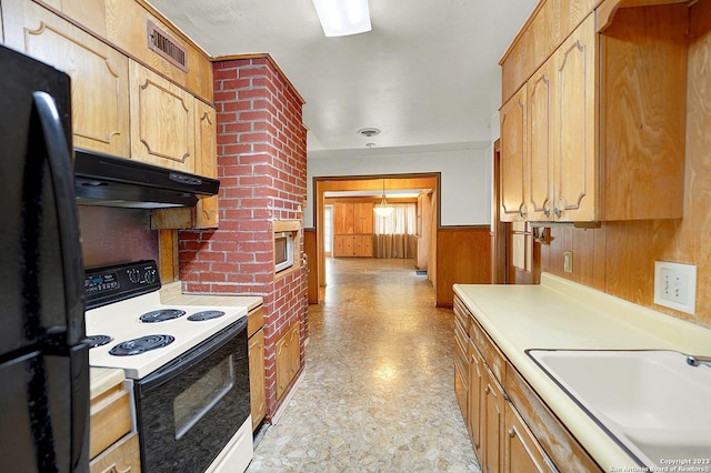 kitchen featuring black refrigerator, sink, wooden walls, and electric stove