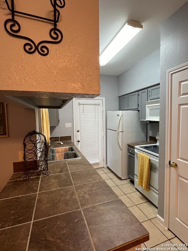 kitchen with gray cabinetry, sink, light tile patterned floors, and white appliances