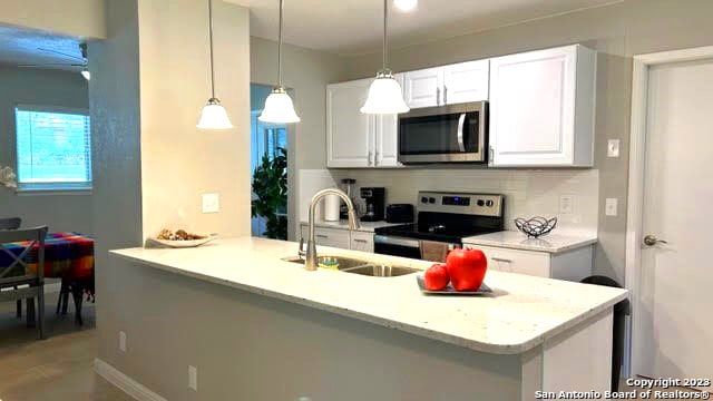 kitchen with white cabinetry, kitchen peninsula, stainless steel appliances, pendant lighting, and sink