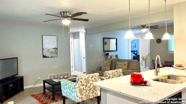 kitchen with decorative light fixtures, ceiling fan, sink, light stone counters, and light tile patterned floors