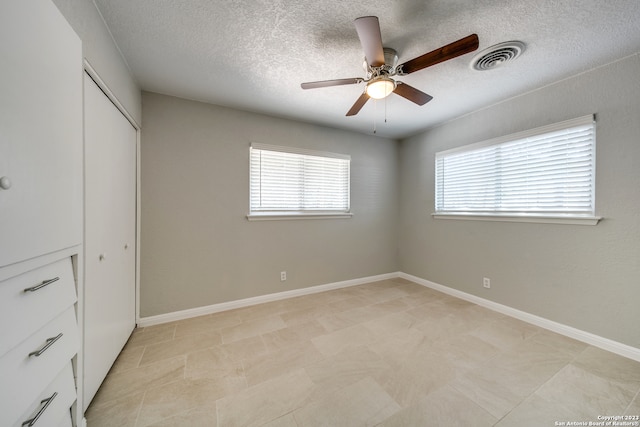 unfurnished bedroom featuring a textured ceiling, a closet, light tile patterned floors, and ceiling fan