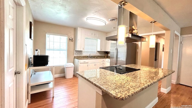 kitchen with white cabinetry, stainless steel refrigerator, pendant lighting, island exhaust hood, and light stone countertops