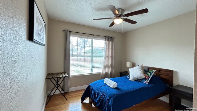 bedroom with a textured ceiling, ceiling fan, and hardwood / wood-style floors