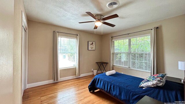 bedroom featuring light hardwood / wood-style floors, multiple windows, a textured ceiling, and ceiling fan