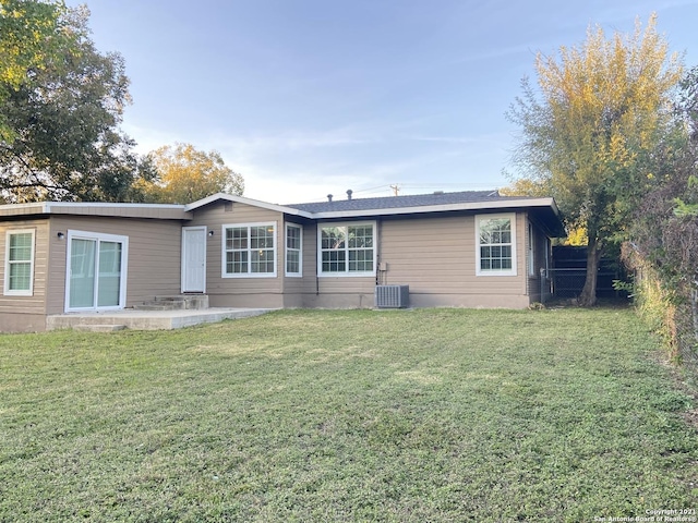 rear view of house with central AC unit and a lawn