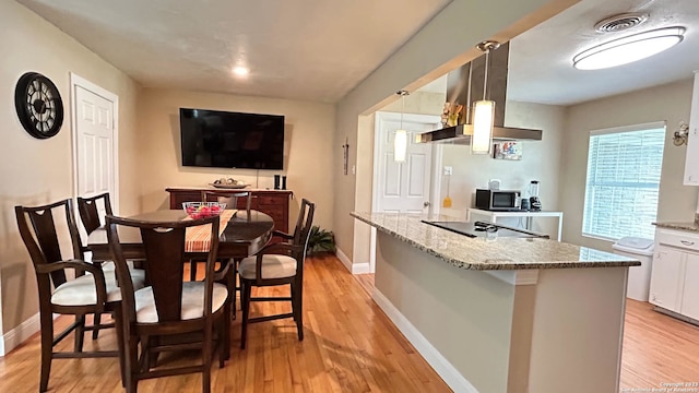 kitchen featuring pendant lighting, white cabinets, light stone counters, black electric cooktop, and light hardwood / wood-style flooring