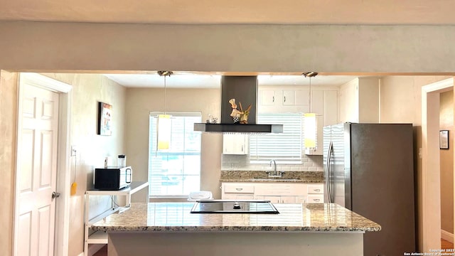 kitchen with wall chimney range hood, white cabinets, black appliances, light stone countertops, and sink