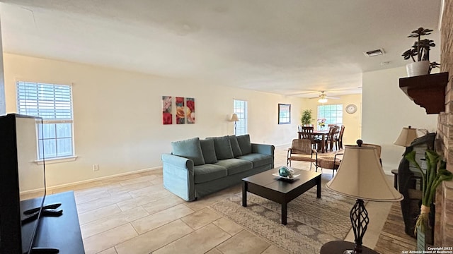 tiled living room with ceiling fan and a stone fireplace